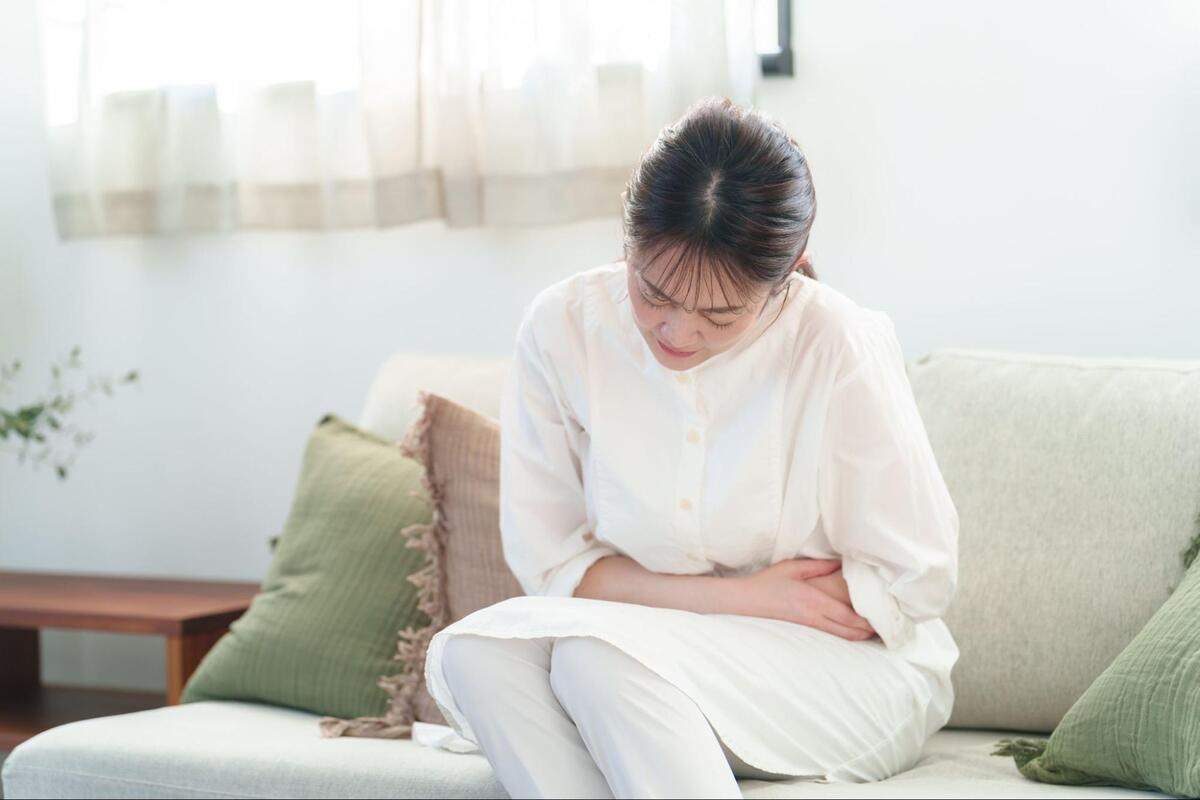 ソファに座り、腹部を押さえて苦しそうにする女性